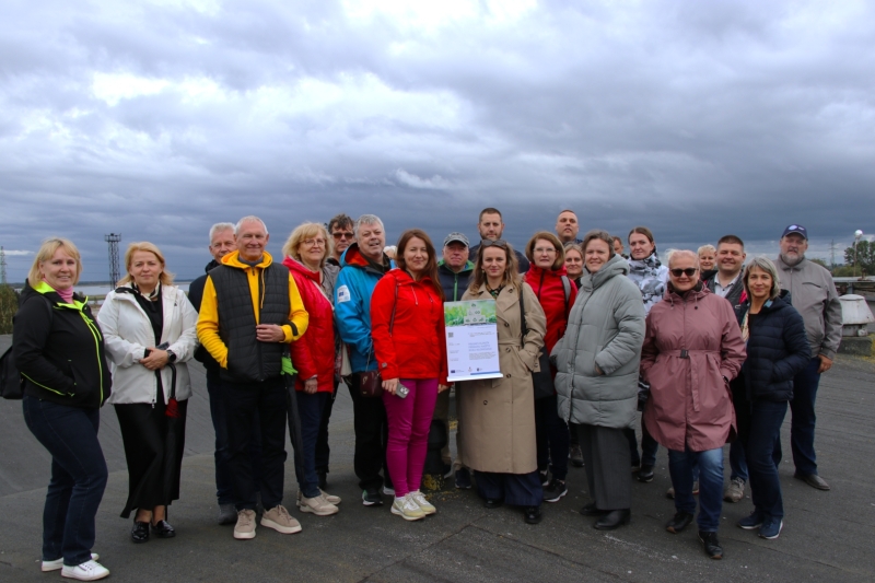Zemgales plānošanas reģiona speciālistu grupa pieredzes apmaiņas pasākumā Liepājas speciālajā ekonomiskajā zonā (SEZ). Dalībnieki kopīgi fotografējas zem mākoņainām debesīm.