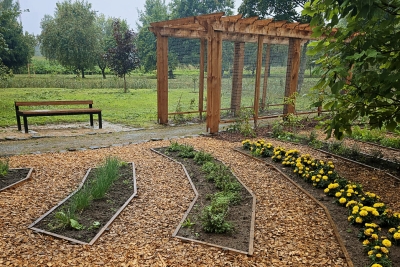 A landscaped garden with wood-chip pathways, herb and flower beds, a wooden pergola, and a bench for relaxation.