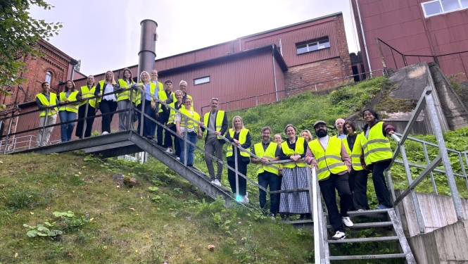 Projekta “Energy Circle” komanda grupas foto Tartu. Dalībnieki atstarojošās drošības vestēs fotografējas uz kāpnēm pie industriālas ēkas.