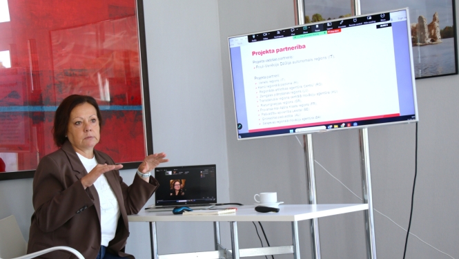 CHERRY” projekta iesaistīto pušu sanāksme. Dalībniece prezentē projekta partnerību un iesaistītās organizācijas no dažādiem Eiropas reģioniem; prezentācija redzama ekrānā.