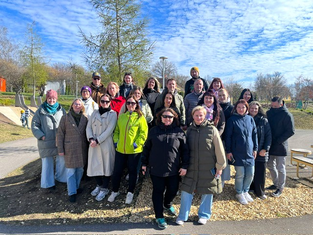 Zemgales reģiona pašvaldību pārstāvju grupa stāv kopīgai bildei ārā Valmieras skeitparkā; cilvēki ģērbušies jakās, fonā redzami koki, celiņi un skeitparka elementi saulainā laikā.