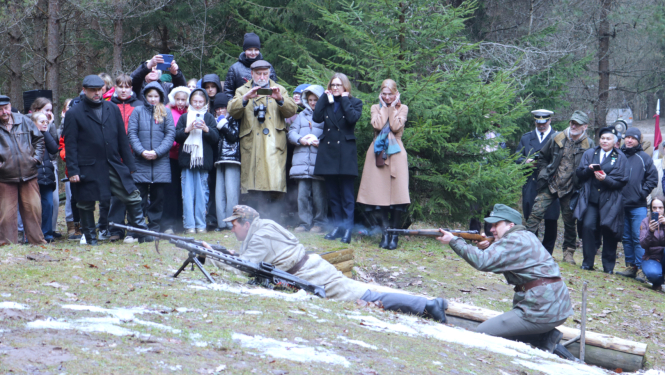 Īles nacionālo partizānu bunkura piemiņas vietā organizētā kaujas rekonstrukcija pulcēja plašu interesentu loku gan no Latvijas, gan Lietuvas, tostarp jauniešus. Attēlā notiek kauju rekonstrukcija, kuru vēro apmeklētāji.